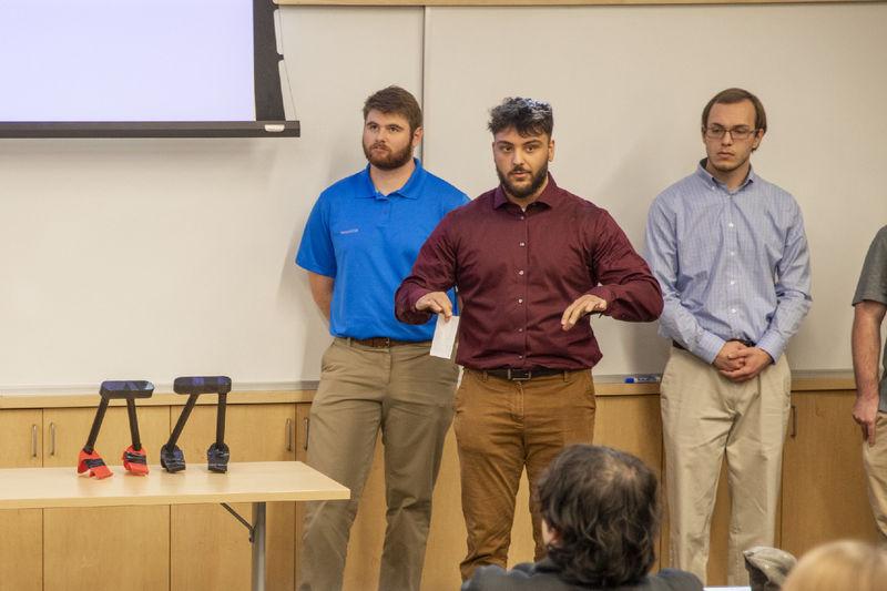 Three male students present portable assistive toilet handles